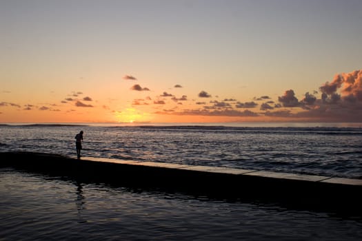 A male fishes off a concrete breakwater at Ha'atafu Beach, Tonga on sunset.