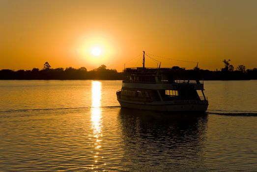 Silhouette of a small boat sailing towards setting sun, with deep orange hue.