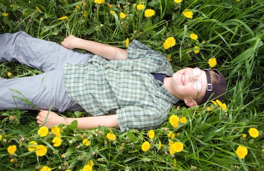 teen boy laying on a beautiful summer dandelion meadow