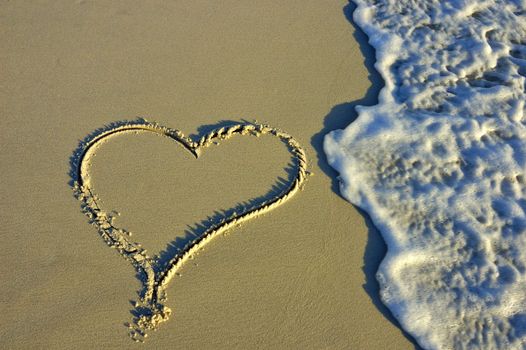 A heart drawn on the beach, in the low evening light, about to be washed away by a wave.