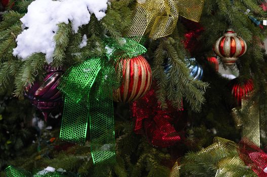 variety of Christmas tree ornaments on a Christmas tree which is outdoors with snow on it also adorned with lights