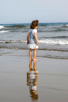 Child is standing on the beach looking at the sea.