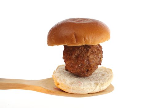 Fresh baked meatball on a bread roll on a wooden spoon aginst a white background