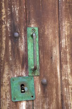 Green metal door handle and keyhole on weathered wooden door.