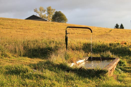 Rustic fountain next to a yellow field in the country by sunset