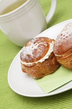 Two profiterole on a plate and a cup of green tea