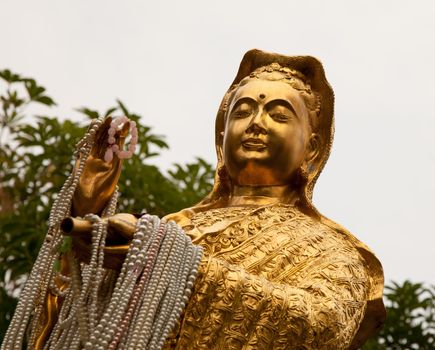 Kuan Yin the avartar of next Buddha statue in gold with pearl lace  from the servants in her hands, Korat, Thailand.