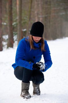 girl in blue coat making a snow ball