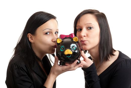 closeup of two young women kissing a piggy bank