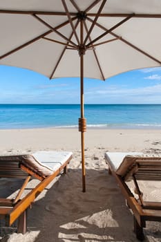 Deckchairs and parasol on the white sand beach facing the lagoon