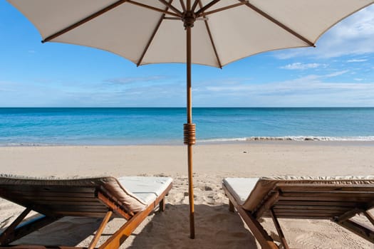 Deckchairs and parasol on the white sand beach facing the lagoon