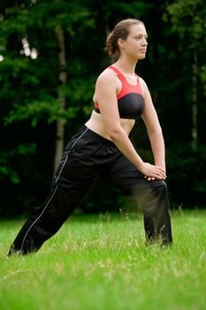 Young adult woman practising yoga on a field surrounded by trees