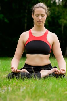 Young adult woman practising yoga on a field surrounded by trees