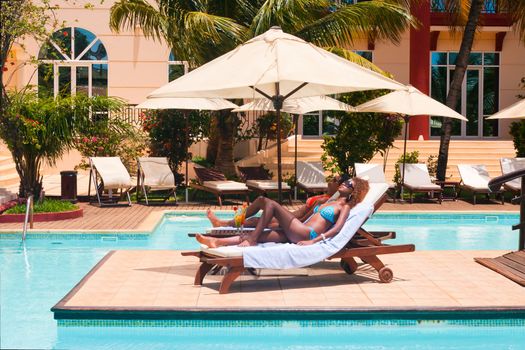 Two women sunbathing on deckchairs by the pool