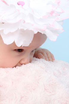 Cute baby girl with a flower hat on a fluffy pink blanket