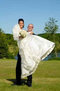 Groom is lifting his bride up in a park.