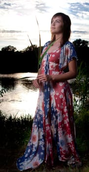 a young woman standing in front of a lake back light from the sun ligthened with flash