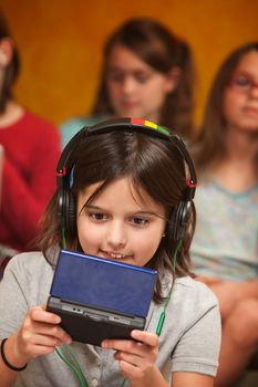 Little Caucasian girl with earphones plays a handheld video game