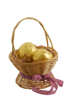 Two eggs wrapped in golden foil in straw interwoven basket with ribbon isolated on white background