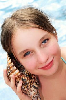 Happy young girl holding a large seashell on tropical beach