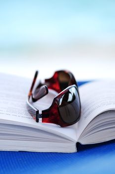 Sunglasses and open book on beach chair - summer vacation concept