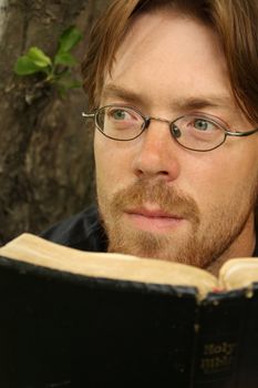 A man reading a Bible and looking thoughtful.