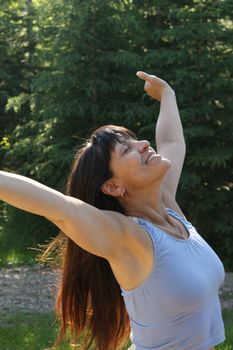 A smiling Aboriginal woman in her 40's stretches in the sun in a forest.