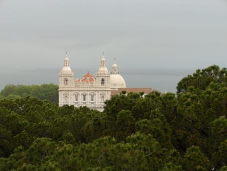 The white walls and terra cotta tile roof of a church in Lisbon, Portugal, rising above treetops.