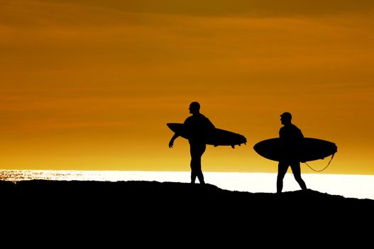 Pair of surfers heading along the cliffs at Santa Cruz for the last ride of the day as the sun sets