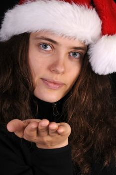Attractive young woman in a santa hat holding hand out for gift over a black background
