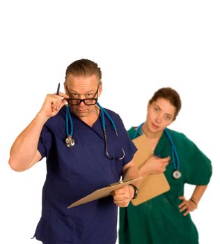 Doctor in forground having just checked chart id questioning with intern standing behind slightly out of focus, both with steoscopes around neck