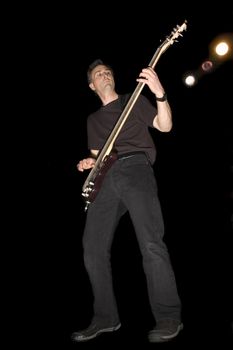 Bass Guitarist playing while isolated on black during live concert