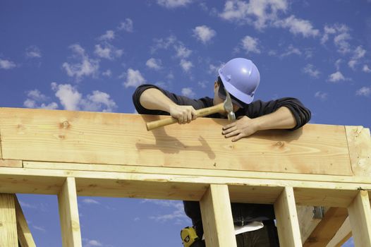 Construction worker pounding in a nail against a blue sky with puffy clouds