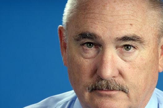 older baby-boomer businessman in closeup over a blue background