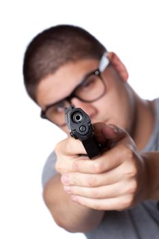An angry looking teenager wearing glasses pointing a black handgun at the viewer. Shallow depth of field.