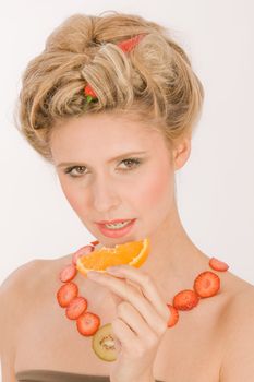 Attractive young blond woman with strawberry-kiwi-chain eating an orange