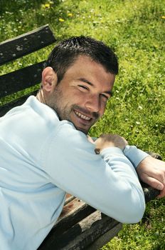 attractivz man is relaxing on a bench in a natural environement