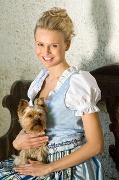 Young Bavarian Dirndl beauty with dog, sitting on a bench