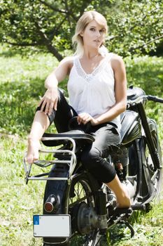 Fashionably dressed woman seated on an old motorcycle