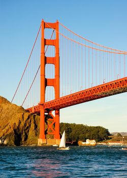 one of the towers of the Golden Gate Bridge from the cabbage patch as a boat goes under it at sunset