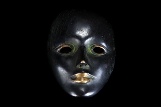 An ancient antique mask, on black studio background.