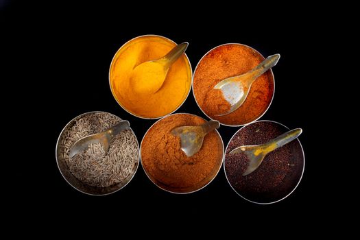 A variety of common spices from an Indian kitchen, on black background.