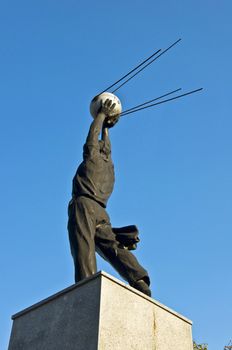 Monument of the first satellite of the Earth. A man holds a satellite in the blue clear sky.