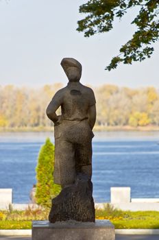 Monument to the peasant girl. Socialist Realism monument in the city embankment against the river and the autumn forest.