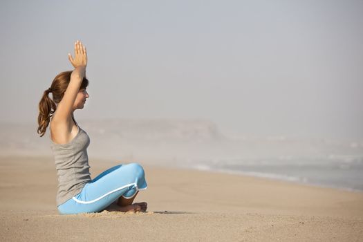 Beautiful young woman on the beach doing yoga exercises