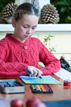 young girl, red knit sweater, drawing with wax pens