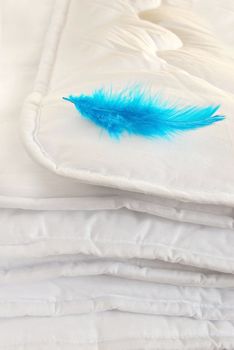 white folded cotton duvet background with blue feather