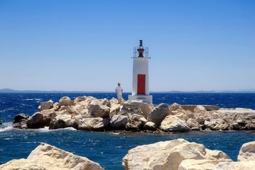 A man standing next to a small light house on a windy day