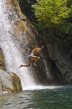 Teenage girl is jumping into the waterfall