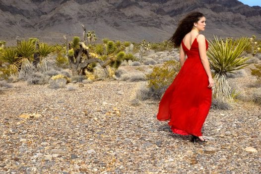 A girl walking in the desert wearing a red silk evening gown and stilettos